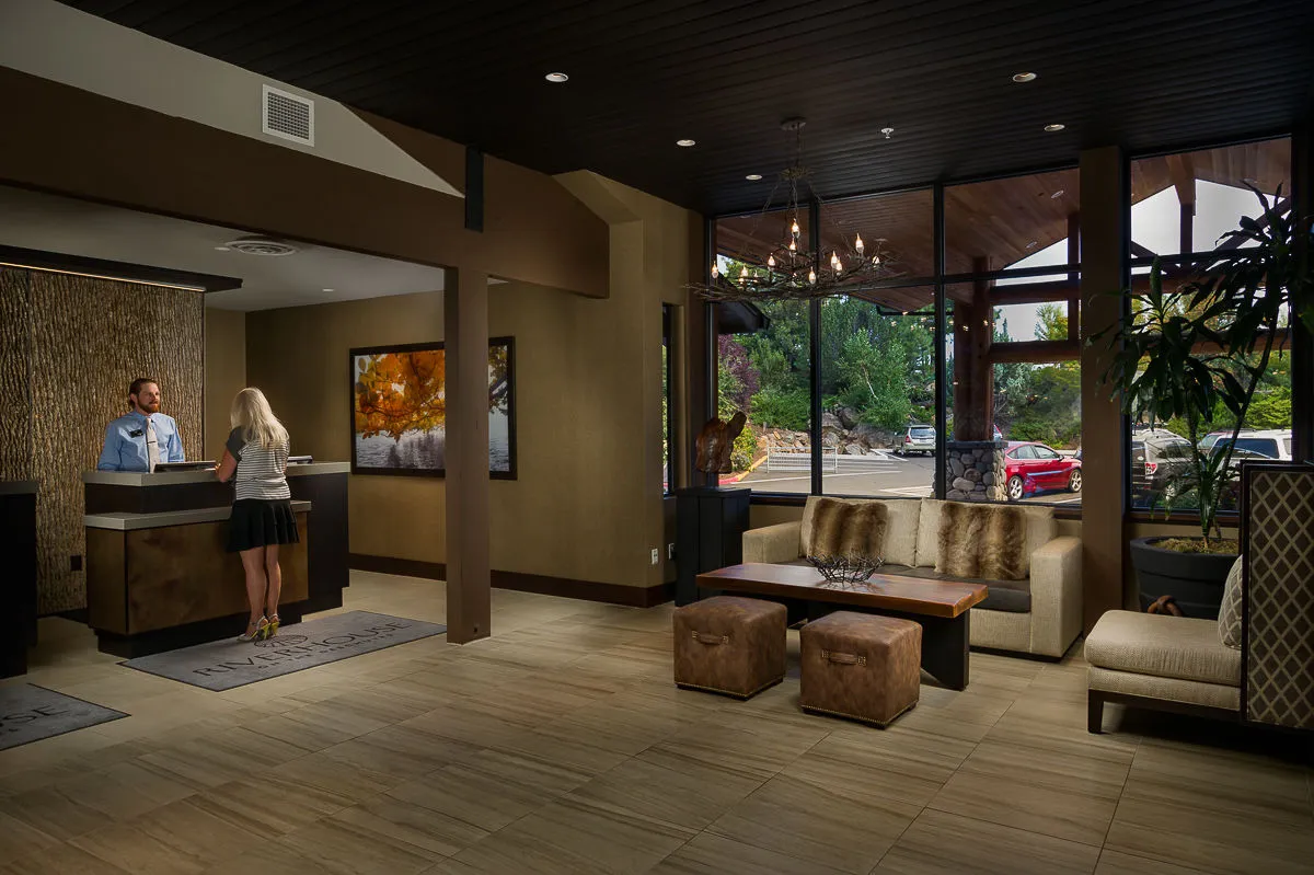 The image shows the inviting lobby area with a stylish reception desk, ample comfortable seating, large windows letting in natural light, and thoughtfully placed artwork. The atmosphere is both relaxing and social, ideal for guests to unwind before or after using amenities like the pool or fitness center.