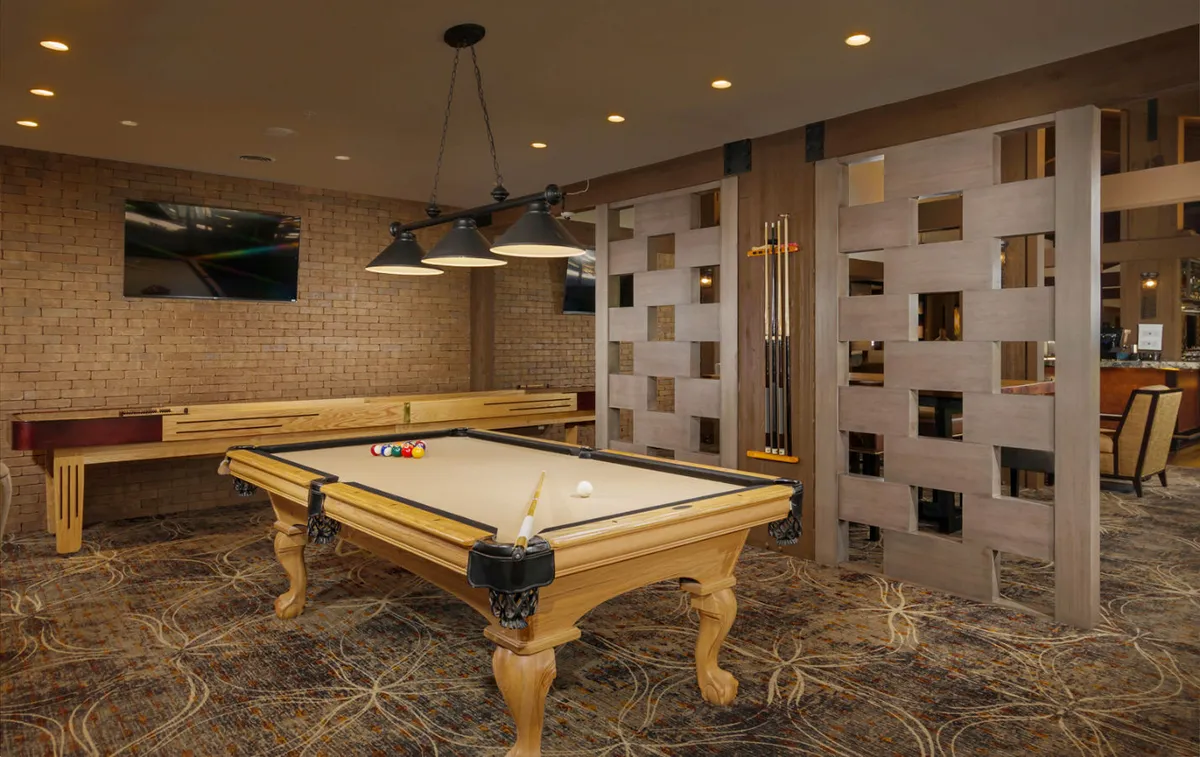 An inviting interior lounge featuring a pool table, hanging lights, decorative wall panels, and a television, creating a casual and social hub within the lodge.