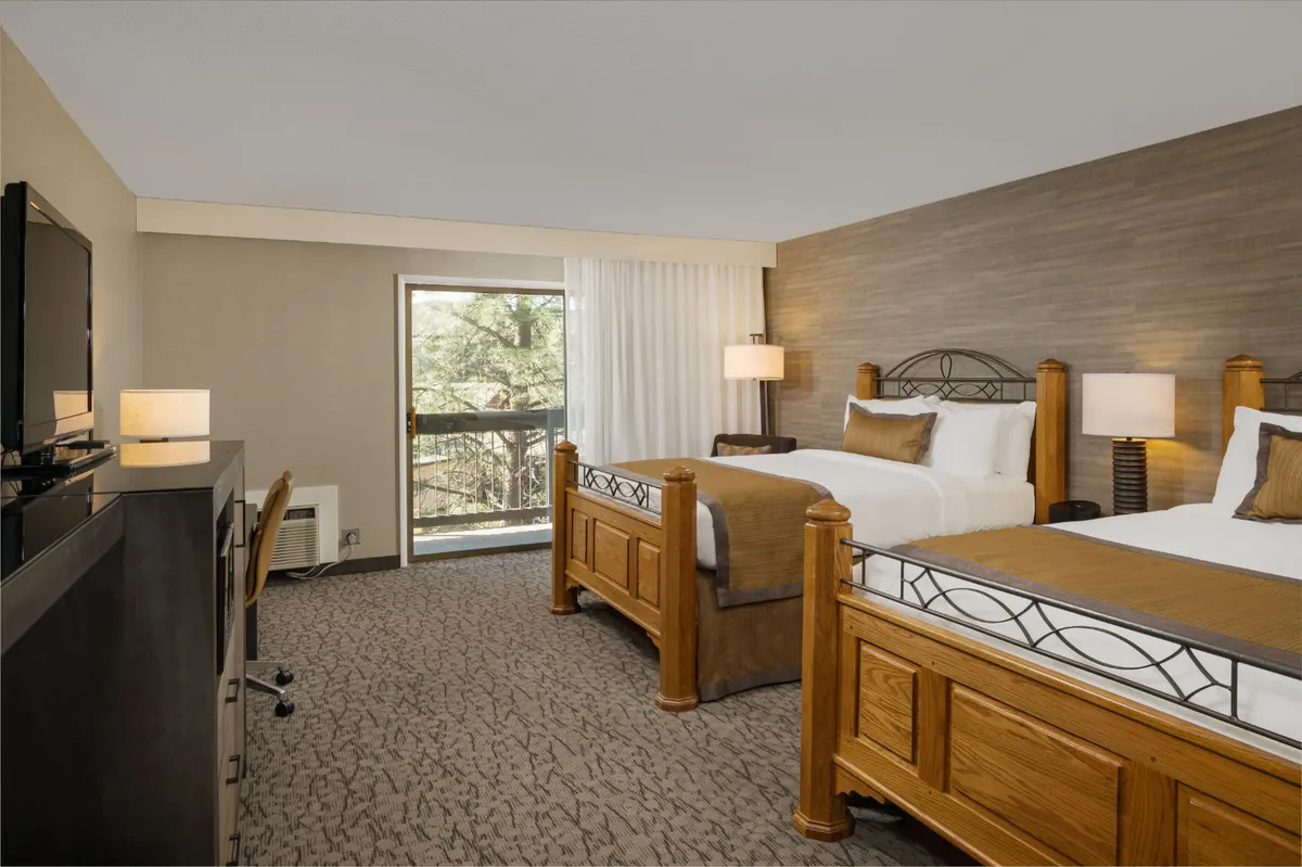 This image offers a different angle of the bedroom, with wooden beds placed near a large window. Natural light pours in, and a television and decorative lamps are present, suggesting both relaxation and entertainment. The window view hints at scenic vistas beyond, complementing the narrative of enjoying river views from inside.